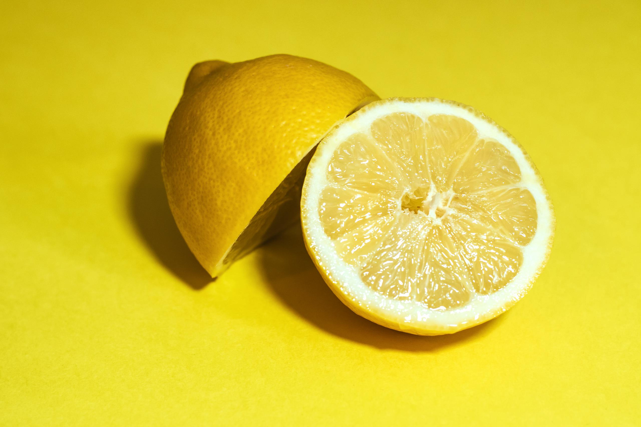 Close-up of a juicy lemon sliced in half, set against a vivid yellow background.